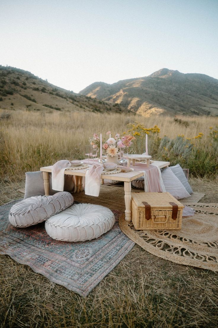 Elegant low picnic table with blush florals, floor cushions and woven rugs set in a golden mountain meadow